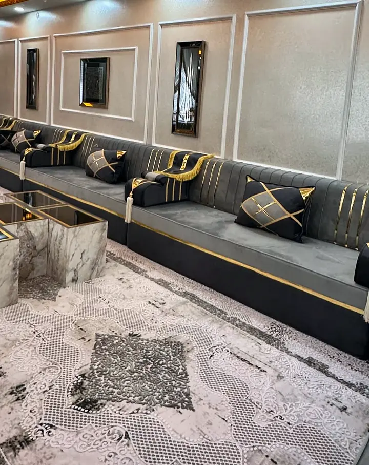 Charcoal and gray seating along a paneled wall, with black pillows crossed by gold straps and a gold-fringed armrest throw