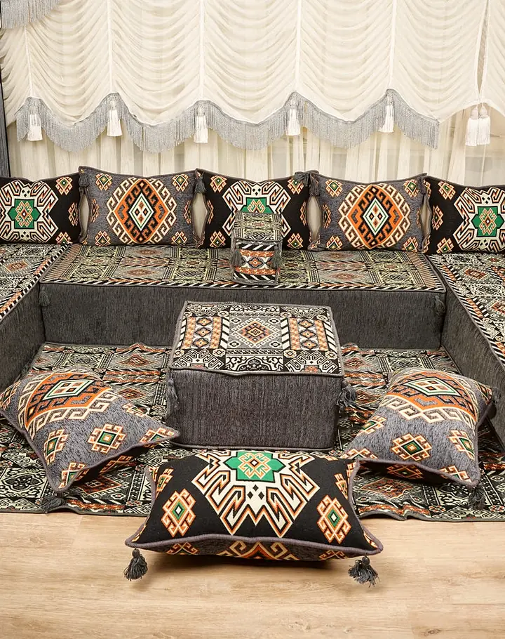 Charcoal and black kilim U-shaped floor sofa with orange and green diamond backrests, a square ottoman and floor pillows on a rug