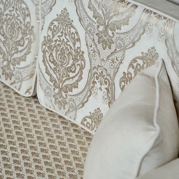 Close view of a cream damask jacquard back cushion resting above a quilted seat, with a velvet accent pillow