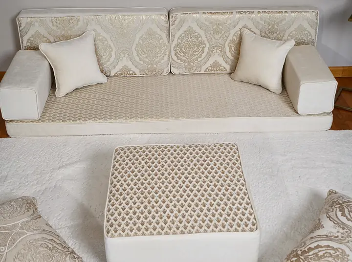Ivory quilted diwan single sofa seen close from the front, with a quilted ottoman and cream damask floor pillows