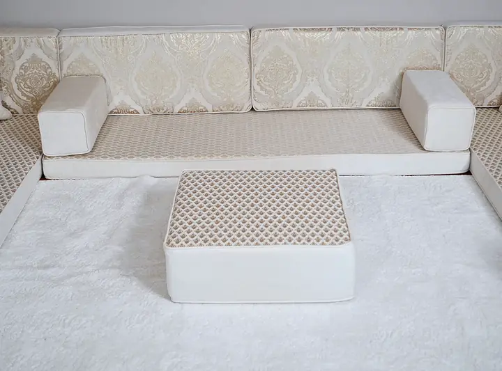 Ivory diwan seating with damask backrests, white box armrests and a quilted ottoman centered on a white shag rug