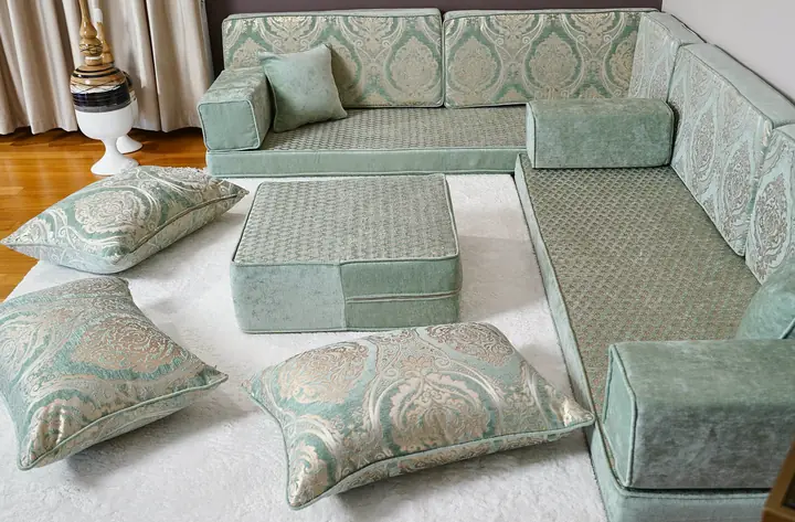 Sea green L-shaped diwan turning a room corner, with a square ottoman and three large floor pillows set in front