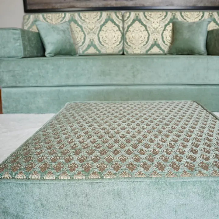 Sea green quilted ottoman in the foreground with the matching diwan floor sofa softly blurred behind it