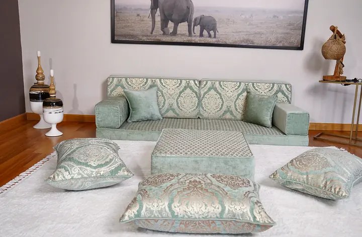 Sea green single diwan floor sofa with a quilted seat, an ottoman and three jacquard floor pillows on a white rug