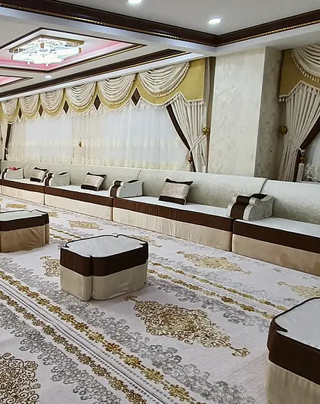 Long reception hall lined on every wall with cream majlis seating trimmed in chocolate brown, low poufs set down a gold-patterned carpet