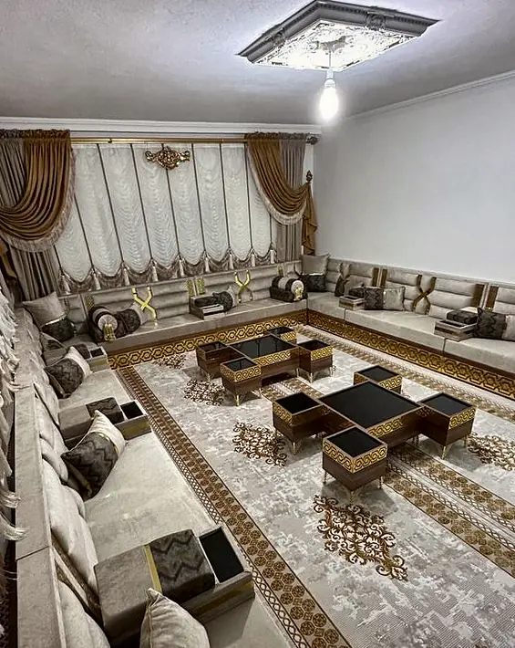 Cream seating along a long room on gold fretwork bases, with chevron pillows and black glass tables under a ceiling rose