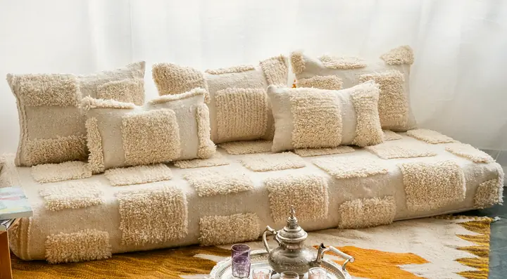 Cream Moroccan floor sofa with textured shag patches and a tea tray resting on a yellow kilim rug in front of the seat