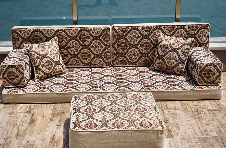 Cream floor diwan patterned with dark brown ogee frames and red tulips, with accent pillows and a matching square pouf on a terrace