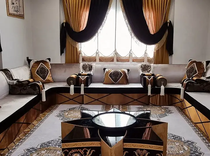 Cream velvet majlis with black bands and gold X-line bases, gold cushions, black and gold drapes, a star table and a large medallion rug