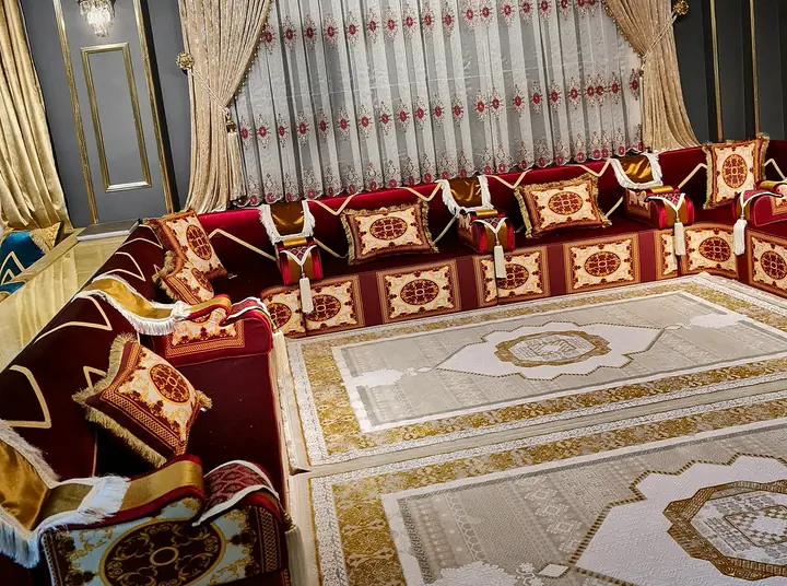 Crimson velvet majlis on every wall with ivory and gold medallion panels on the bases, tasseled bolsters and two cream and gold rugs
