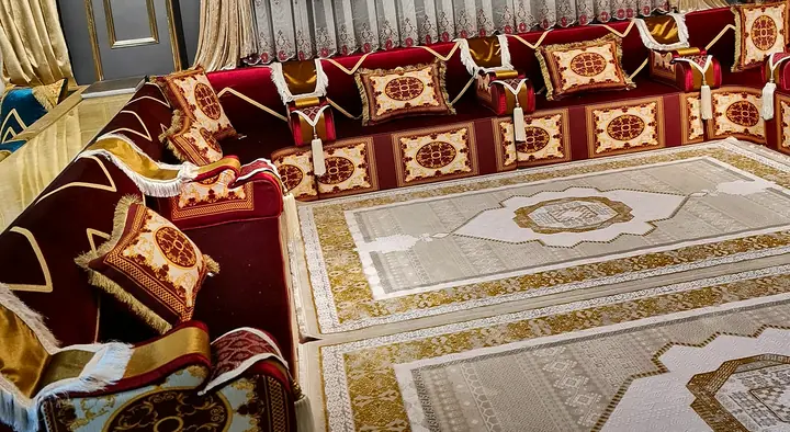 Crimson velvet majlis on every wall with ivory and gold medallion panels on the bases, tasseled bolsters and two cream and gold rugs