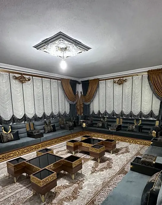 Charcoal gray majlis with gold accents around low black glass tables, under white festoon curtains, gold drapes and a ceiling medallion