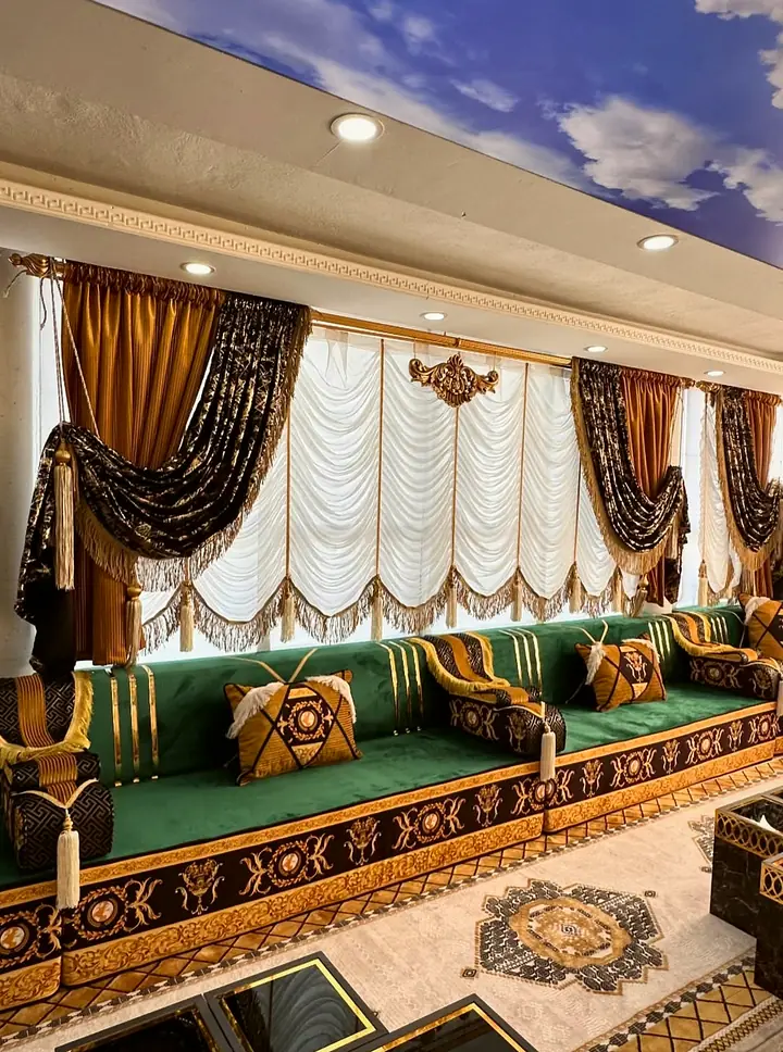 Green velvet seating under balloon curtains, with gold-striped backrests, crest pillows and a fringed bolster at the corner
