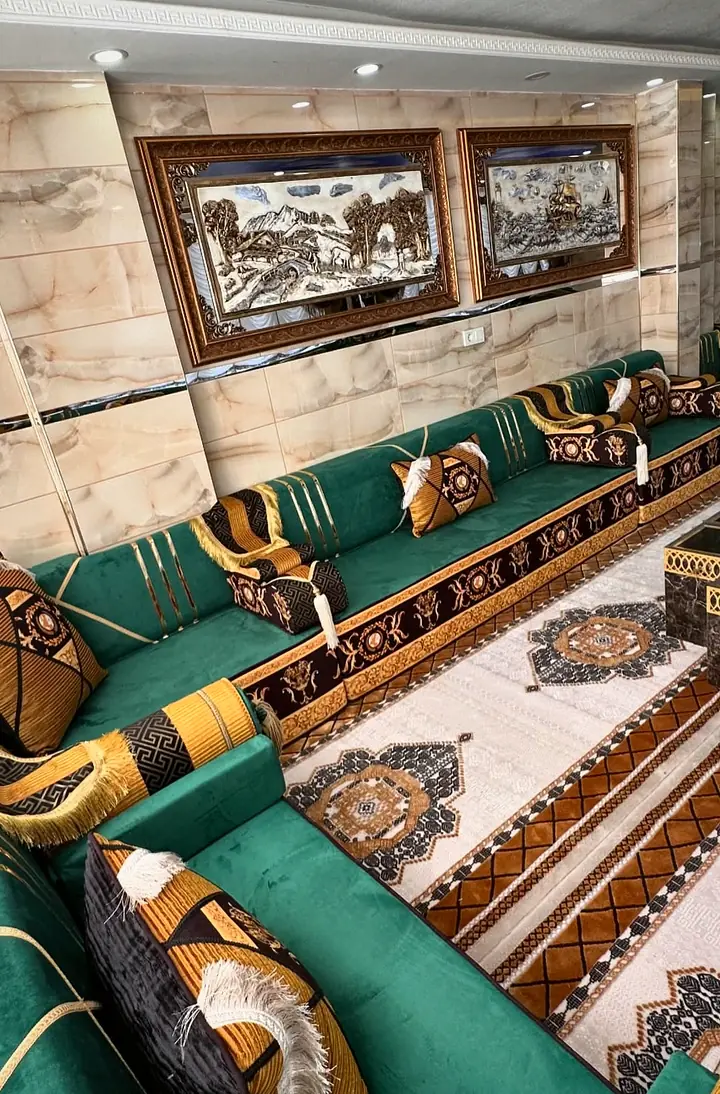 Long run of emerald seats with gold-striped backrests below framed landscape panels, beside a rug with dark medallions