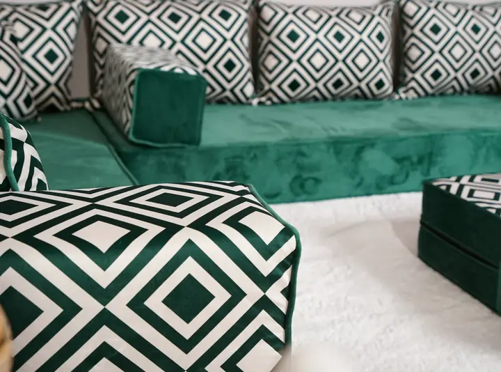 Emerald velvet floor sofa with green and white geometric backrests and bolsters, and a matching ottoman on a white rug