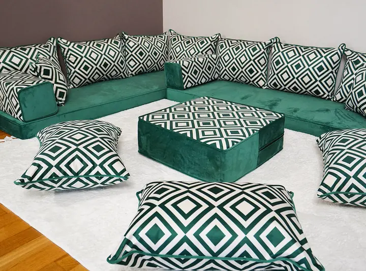 Emerald velvet L-shaped floor couch with green-and-white diamond trellis pillows, an ottoman and floor pillows on a white rug
