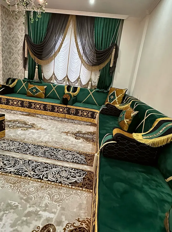 Corner of an emerald velvet majlis with black and gold baroque base bands, fringed armrests and swagged green curtains
