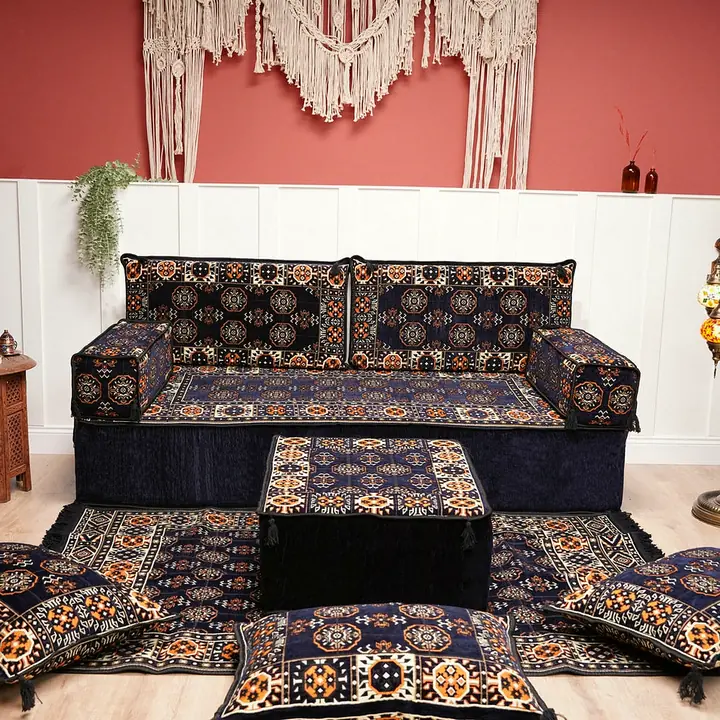 Navy floor sofa with gul medallion backrests, a matching ottoman and floor pillows on a patterned rug below a macrame wall hanging