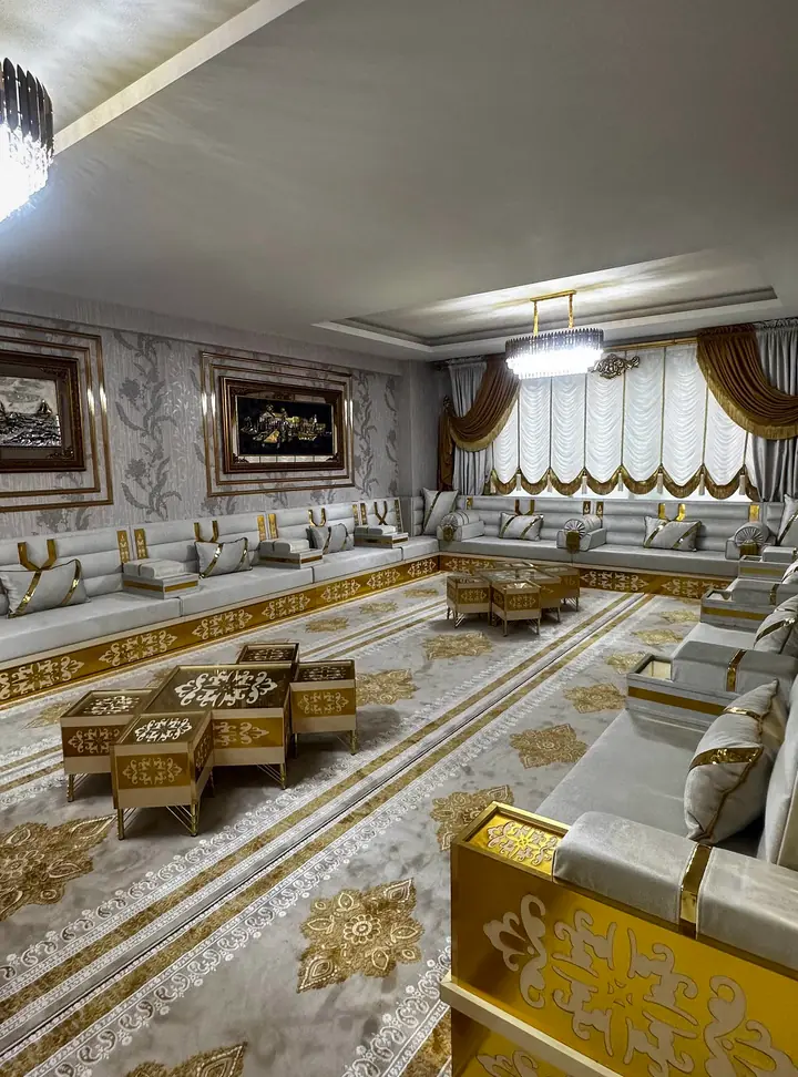 Gilded armrest panel with cut-out scrolls closing a pale gray run, with cushions leaning on the backrests behind it