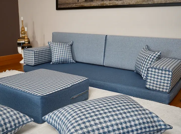Angled view of a light blue floor couch with large check floor pillows and a gingham ottoman placed in front