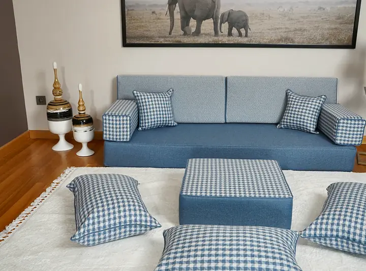 Wide view of a light blue single floor sofa set with a gingham ottoman and floor pillows in a bright room