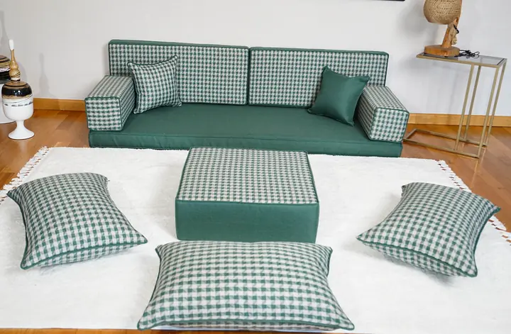 Green single floor couch with green and white gingham back cushions, a check ottoman and floor pillows in front