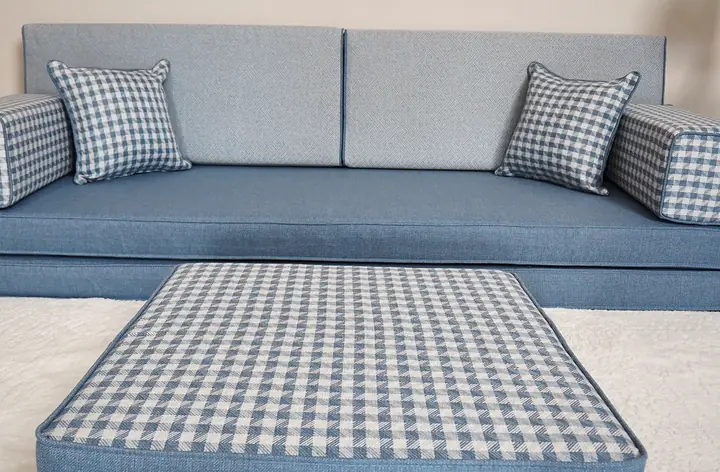 Gingham check ottoman top in the foreground with the light blue linen-look single floor sofa standing behind it