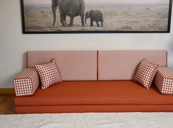 Front close view of a terracotta linen-look floor sofa with soft coral backrests and gingham armrest pillows