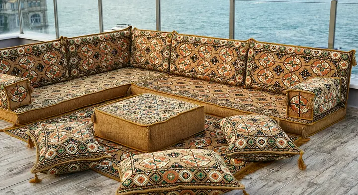 Gold Afghan Gul L-shaped floor sofa with medallion rows, a square ottoman and four floor pillows on a terrace by the water
