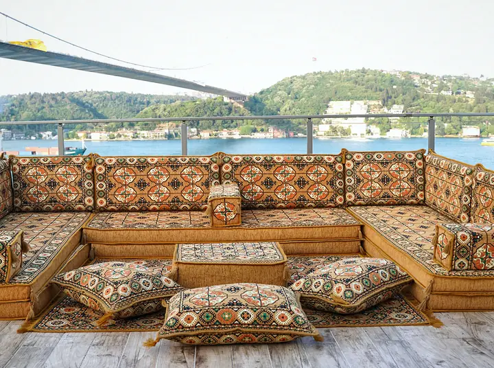 Gold Afghan-pattern U-shaped toshak-style floor couch with an ottoman and floor pillows arranged on an open terrace