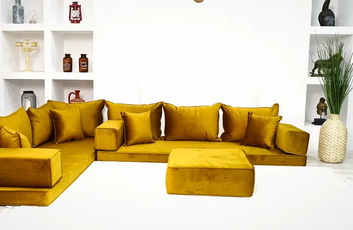 Gold velvet corner seating with plain rectangular backrests, matching armrest blocks and an ottoman on a pale rug