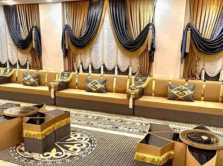 Gold velvet majlis with black-and-gold armrests facing star-shaped tables trimmed with gold fringe, black swag curtains behind