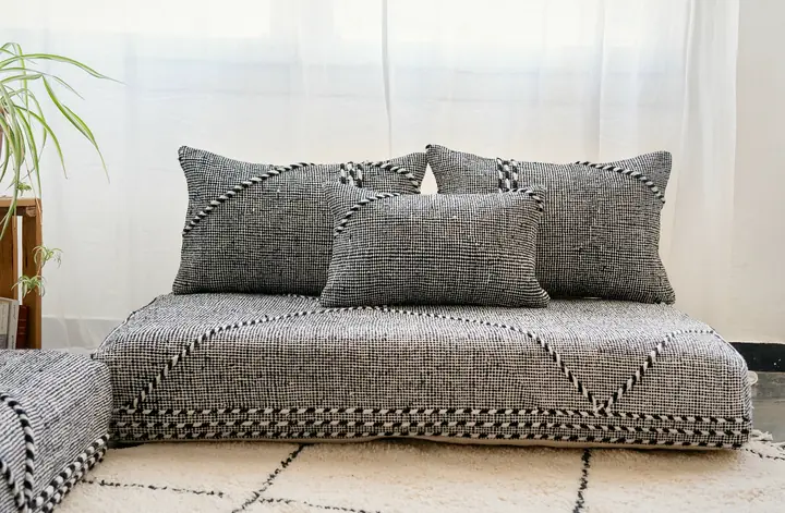 Gray and black woven Moroccan-style floor sofa lined with three matching pillows and set directly on a white rug