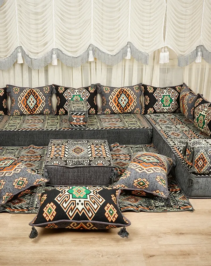 Gray U-shaped floor sofa set in a black, orange and green kilim pattern with an ottoman and tasseled floor pillows on a matching rug