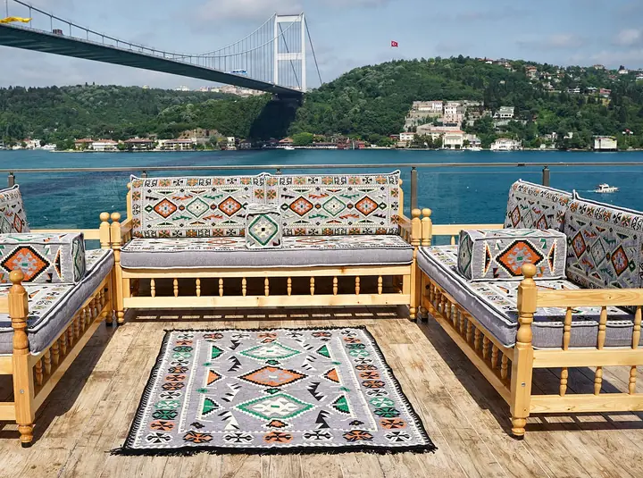 Three pine bench sofas facing a gray kilim rug, with matching patterned backrests and bolster armrests on a sunny wooden deck