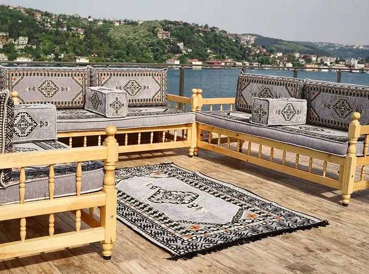 Gray kilim cushions on a U-shaped set of light wooden benches with a matching rug, laid out on an outdoor wooden deck