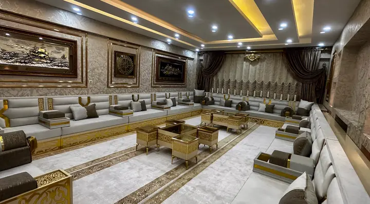 Gray and white majlis on three walls with gold cross straps, gold armrest panels and a cluster of gold-framed low tables