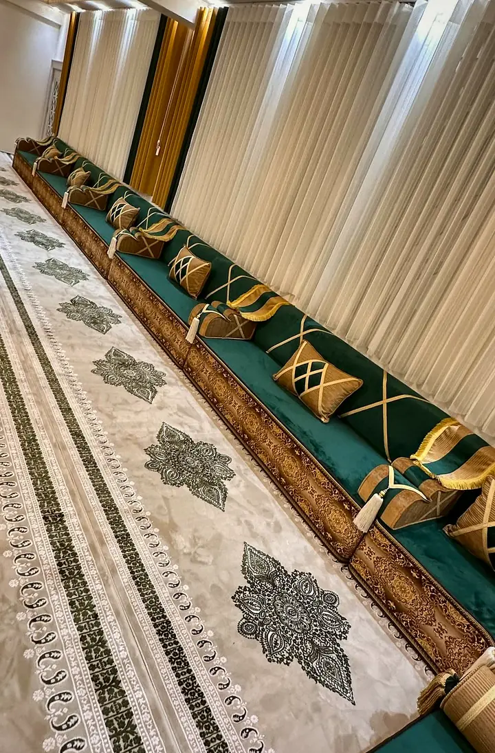 Long green majlis run with caramel-edged seats and rolled armrests beside an ivory rug with dark lace-like medallions