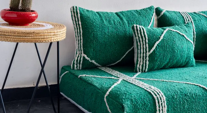 Green Moroccan-style floor couch with white line patterns, backrest and lumbar pillows beside a metal side table with a potted cactus