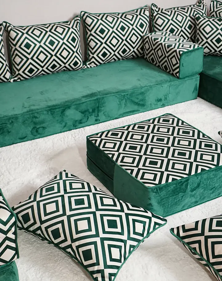 Emerald green velvet U-shaped floor majlis with black-and-white diamond-pattern pillows, a square ottoman and floor pillows on a white rug