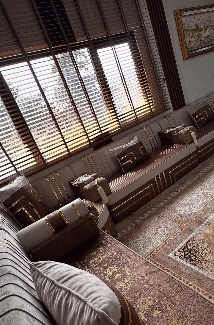 Brown and greige majlis along a sunlit window wall, seen from the corner across a patterned beige rug