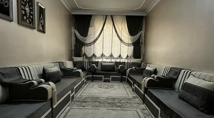 Narrow room seated on three walls with a charcoal and pale grey striped majlis, fringed pillows and a long patterned runner in the middle