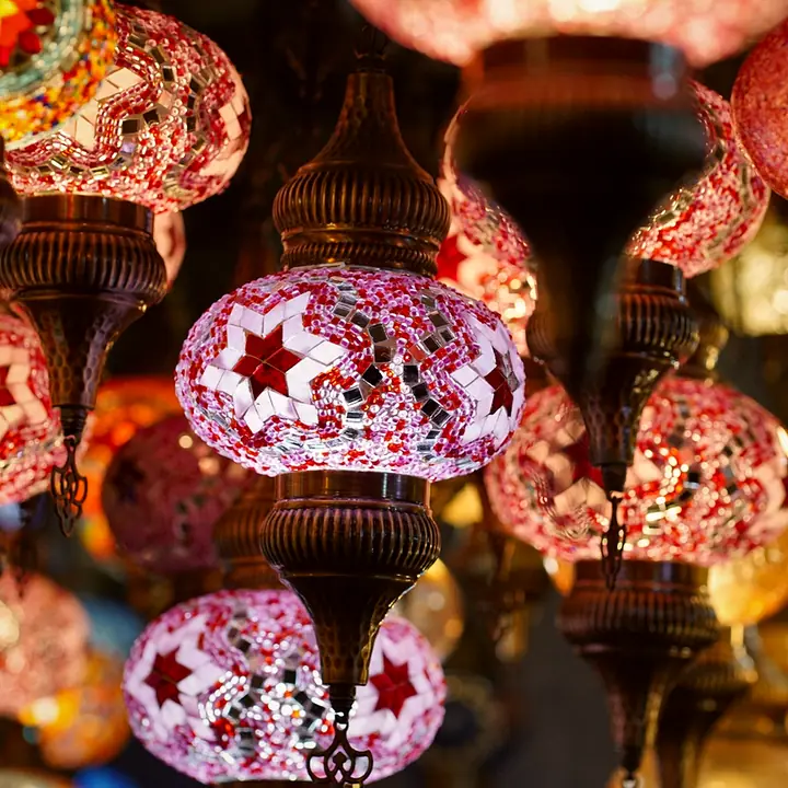 Hanging mosaic lanterns in pink, amber and red glass, all lit and glowing close together in a cluster