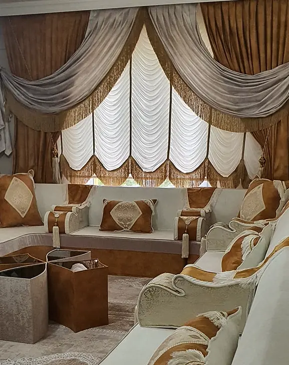Ivory majlis with caramel fringed throws on the armrests, square caramel side tables and white festoon blinds with gray swags
