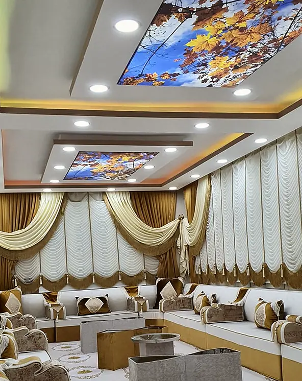 Ivory majlis seats on a caramel base with scrolled velvet armrests and gold cushions, under printed autumn-leaf ceiling panels