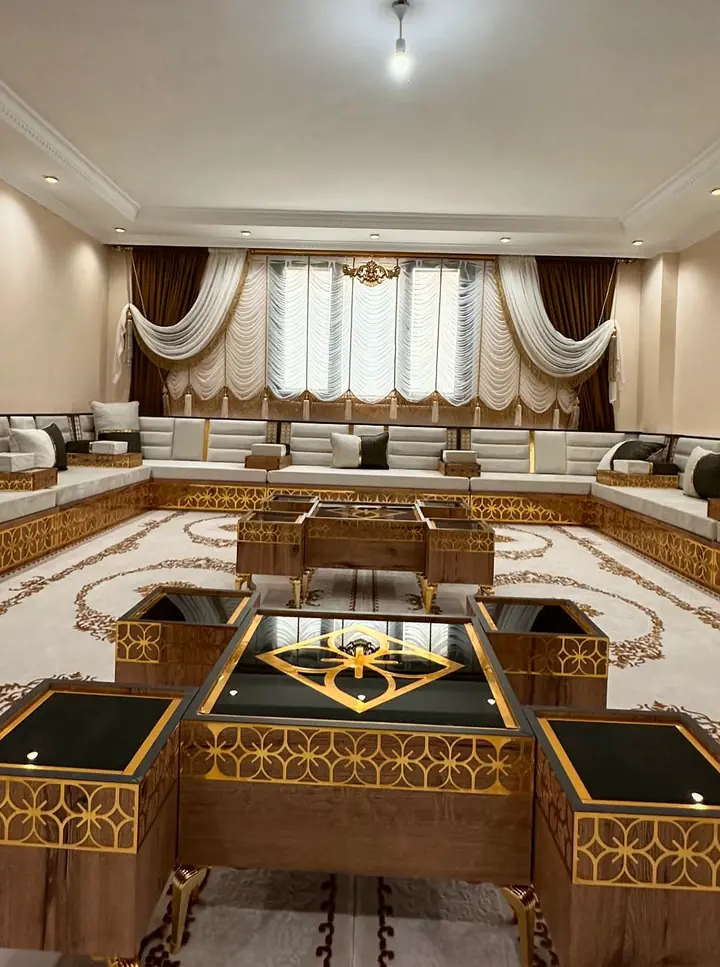 U-shaped ivory seating along three walls of a cream room, with a star-patterned walnut and gold table set on a medallion rug