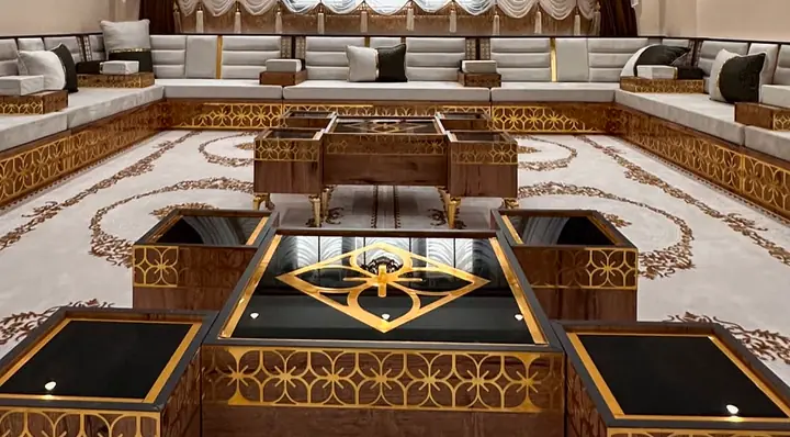 Ivory channel-tufted majlis along three walls of a large room, on walnut and gold lattice bases, with wooden tables on a cream rug