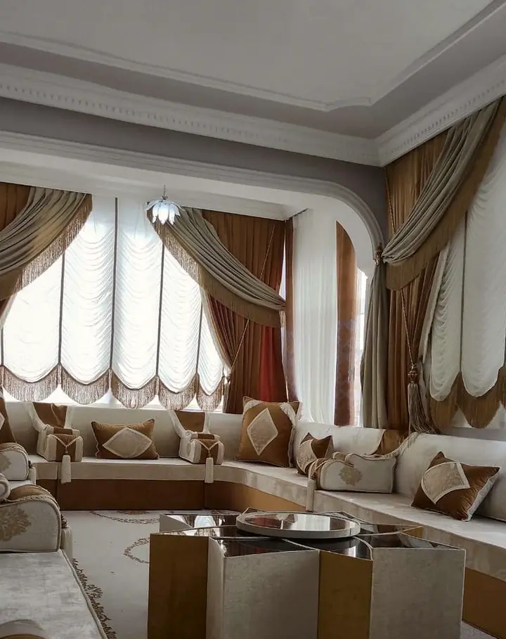 Ivory velvet majlis around three walls under an arched window, caramel diamond-panel cushions and a gold and ivory star table on a pale rug
