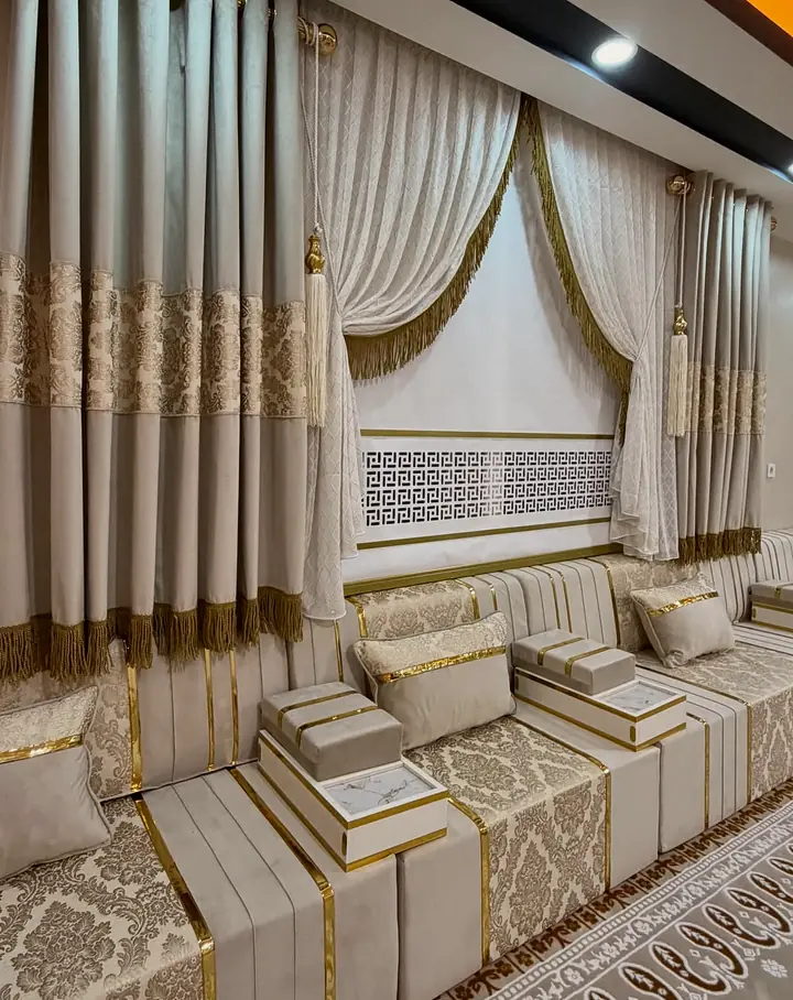 Ivory damask seating under a window with gold-fringed curtains, a Greek-key panel and box armrests topped with marble-look slabs