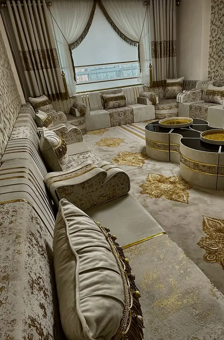 Ivory seat run with gold-leaf print on the bases and a fringed cushion, receding toward linked drum tables and a draped window